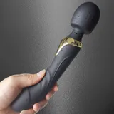 Black Dual Head Vibrator held against a grey wall, showing water droplets on the back of the head and handle