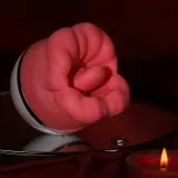 Red rose-shaped vibrator on a mirrored surface beside a lit candle, with droplets around its white base