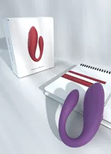 Purple Whale tide vibrator beside a notebook and a white retail box displaying the red colour option